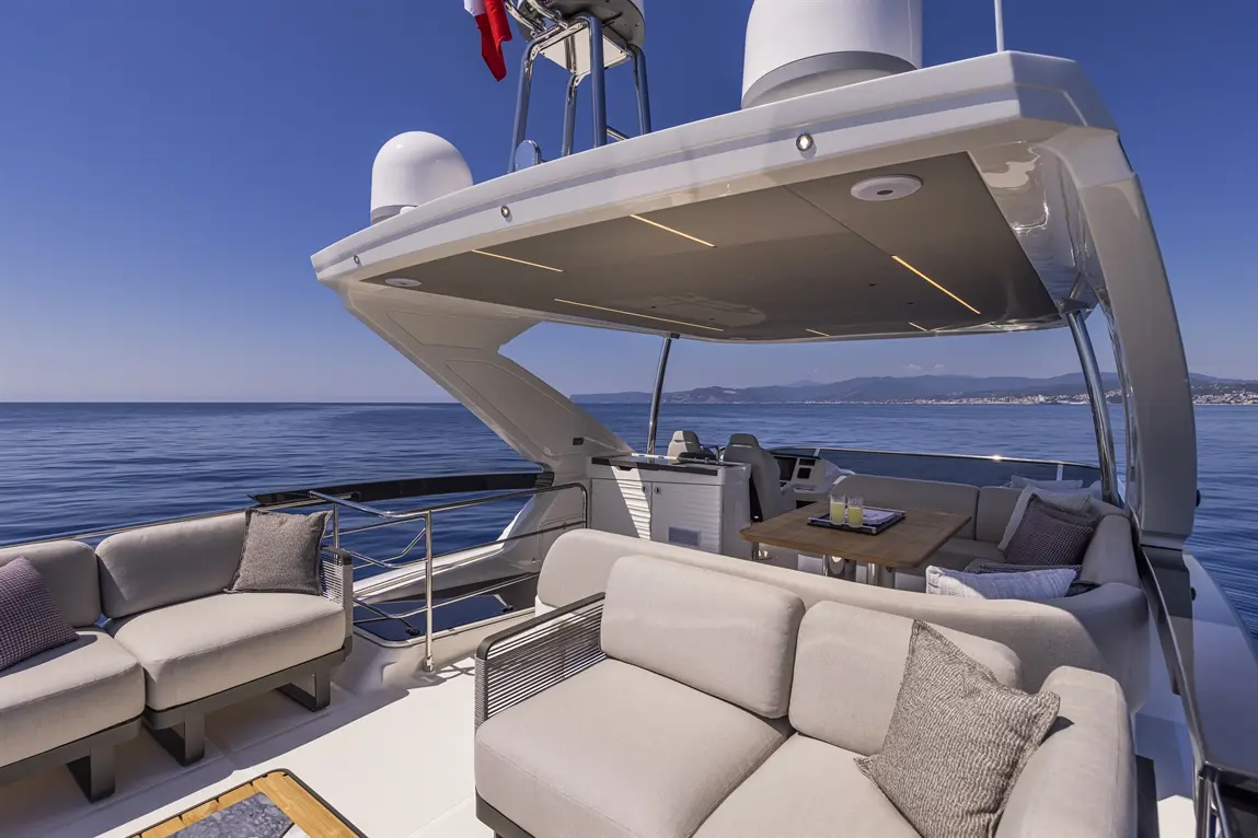 Luxury yacht deck featuring plush seating, a wooden table, and drinks, with serene ocean views and a clear blue sky.
